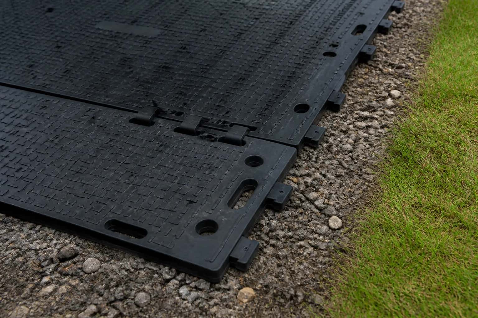 Ground protection mat connection details beside gravel and grass.