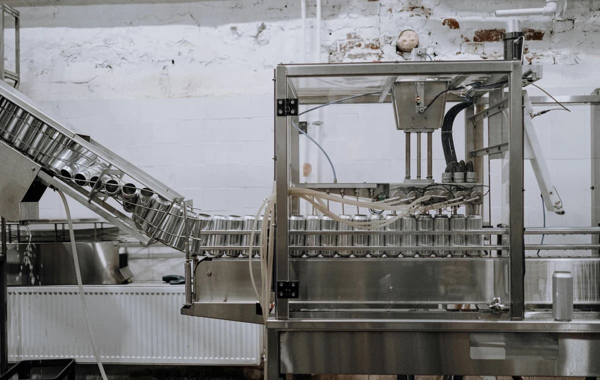 Automated canning line with tin-coated containers moving past filling and sealing stations.
